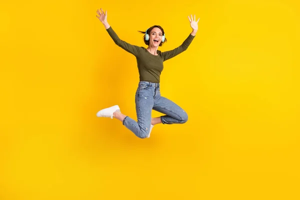 Foto de cuerpo completo de niña salto escuchar música auriculares inalámbricos desgaste suéter aislado sobre fondo de color amarillo brillante —  Fotos de Stock