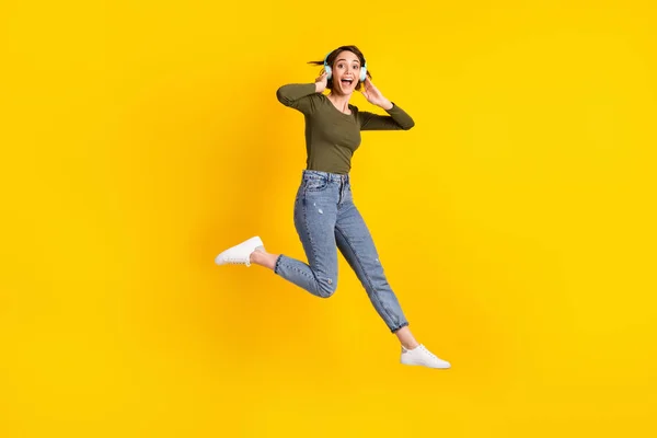 Foto de tamaño completo de niña loca saltar escuchar música en los auriculares desgaste suéter aislado sobre el brillo de color amarillo de fondo —  Fotos de Stock