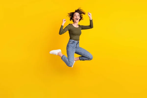 Foto de longitud completa de la chica extática salto levantar los puños usar suéter gumshoes aislado en el brillo de color amarillo de fondo — Foto de Stock