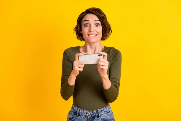 Фото смешной юной леди держать телефон укуса губы зубастый улыбка волнение носить зеленую рубашку изолированы ярко-желтый цвет фона — стоковое фото
