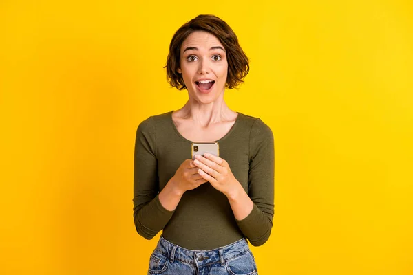 Foto van mooie jonge meisje houden mobiele telefoon open mond verrast gezicht dragen groen shirt geïsoleerde levendige gele kleur achtergrond — Stockfoto
