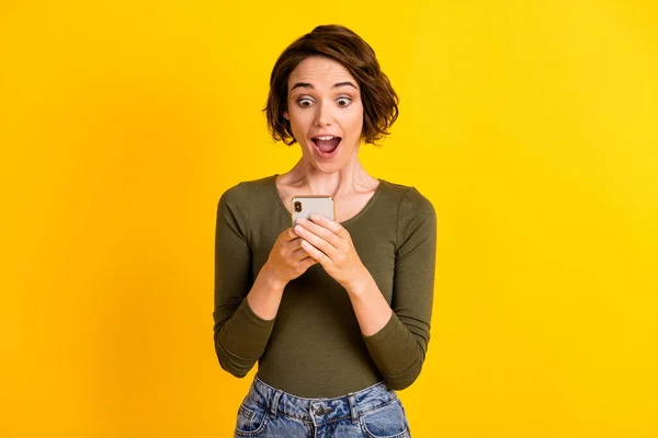 Foto de chica bonita mantenga la pantalla de aspecto del teléfono inteligente cara asombrada boca abierta desgaste camisa verde aislado vívido color amarillo fondo — Foto de Stock