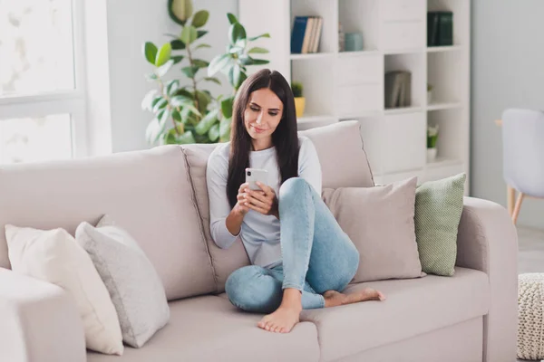 Полная длина фото сосредоточены довольно привлекательной молодой женщины сидеть диван расслабиться читать сообщения смартфон в помещении дома — стоковое фото