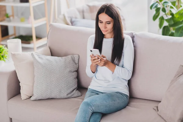 Fotografie z vážné krásné sladké okouzlující mladá žena nosit bílý jumper sedět pohovka číst blog uvnitř v domácím obývacím pokoji — Stock fotografie