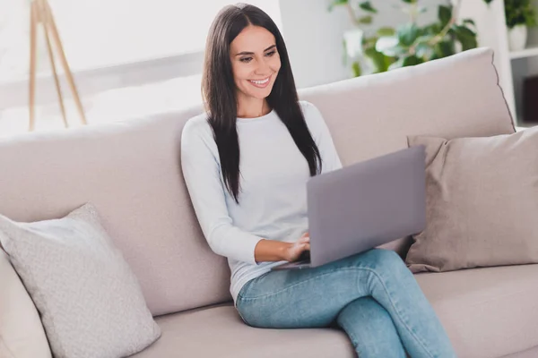 Фото позитивной счастливой женщины в чате на ноутбуке сидеть диван выходные дома свободное время в доме в помещении — стоковое фото