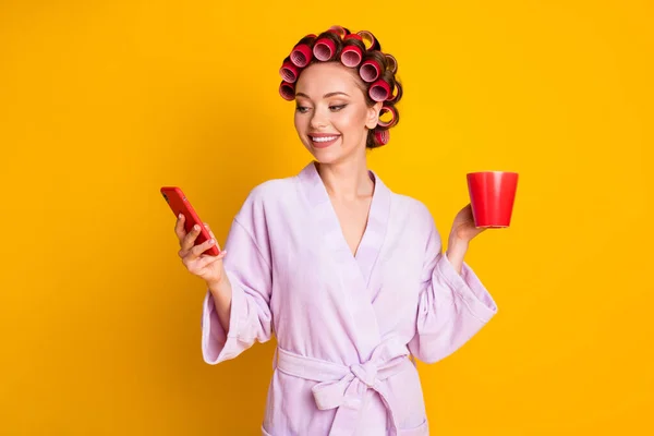 Portrét krásné soustředěné veselá žena na sobě natáčky pití latté pomocí zařízení izolované přes jasně žluté barvy pozadí — Stock fotografie