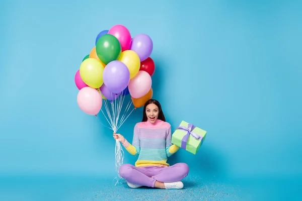 Foto de tamaño completo de chica asombrada sentarse piso celebrar muchos globos caja de regalo desgaste suéter aislado color azul fondo — Foto de Stock
