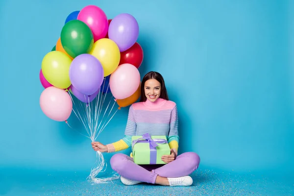 Foto de longitud completa de niña bonita sentarse piso piernas cruzadas celebrar globos caja de regalo desgaste jersey aislado color azul fondo — Foto de Stock