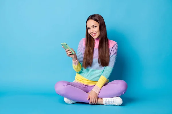 Retrato de chica atractiva alegre sentada posición de loto piernas cruzadas utilizando dispositivo aislado sobre fondo de color azul brillante — Foto de Stock