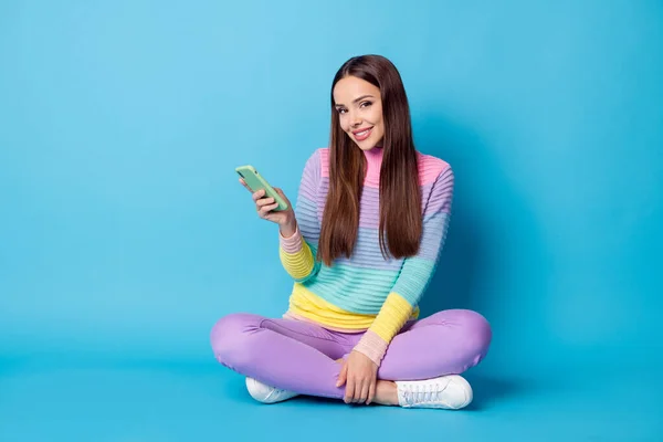 Portret van aantrekkelijke vrolijke meisje zitten lotus positie gekruiste benen met behulp van apparaat geïsoleerd over helder blauwe kleur achtergrond — Stockfoto