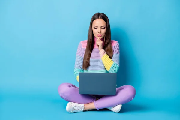 Potret gadis pintar yang menarik dan fokus yang duduk di posisi teratai menyilangkan kaki menggunakan laptop yang belajar terisolasi dengan latar belakang warna biru cerah — Stok Foto