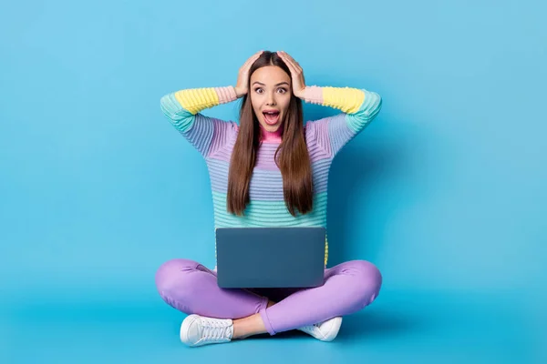 Retrato de alegre chica sorprendida sentada posición de loto piernas cruzadas utilizando portátil grandes noticias aisladas sobre fondo de color azul brillante — Foto de Stock