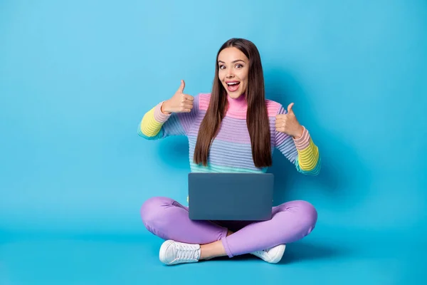 Retrato de menina alegre agradável sentado posição de lótus cruzado pernas usando laptop mostrando polegar isolado sobre fundo de cor azul brilhante — Fotografia de Stock