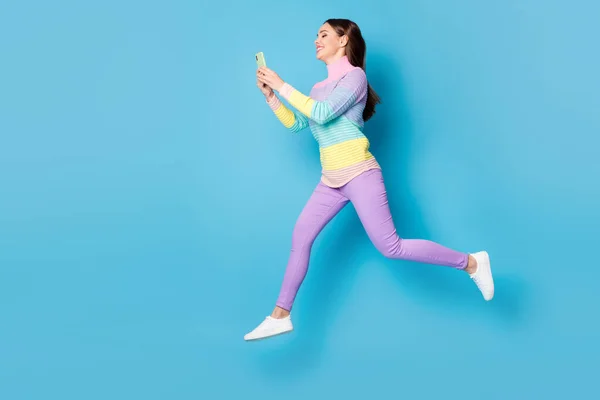 Full längd kroppsstorlek bild av trevlig fokuserad glad flicka hoppa med hjälp av cell app 5g promenader chatta isolerad på klarblå färg bakgrund — Stockfoto