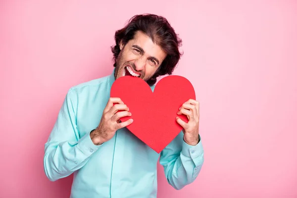 Photo portrait of guy biting big red heart card isolated on pastel pink colored background — Stock Photo, Image