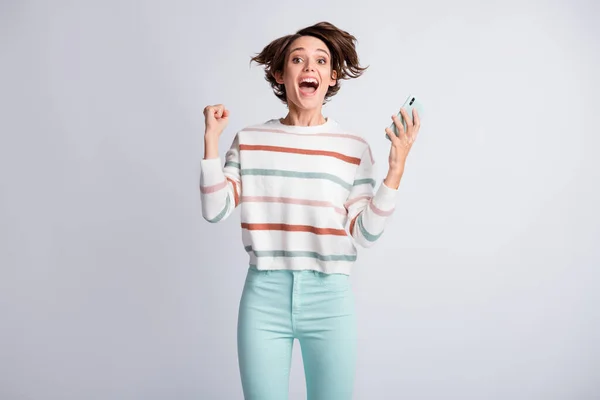 놀란 젊은 아가씨가 줄무늬 스웨터를 입고 있는 사진 현대 장치 상승 주먹 분리 회색 배경 — 스톡 사진