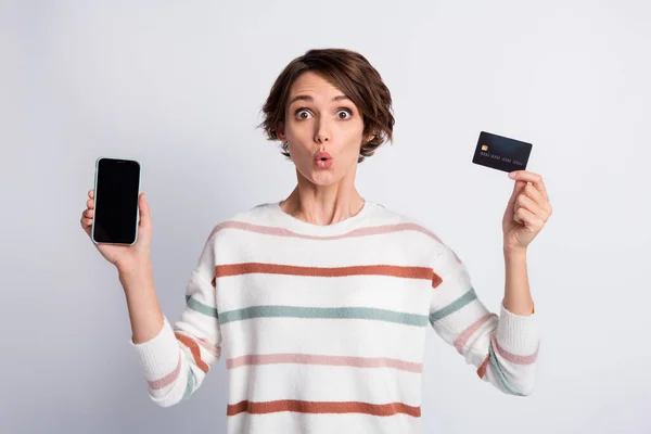 Фото здивованої смішної молодої жінки, одягненої в смугастий пуловер, що тримає сучасний пристрій кредитної картки ізольованого сірого кольору фону — стокове фото