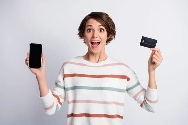 Photo of impressed young lady wear striped sweater holding modern gadget bank card isolated grey color background — Stock Photo, Image