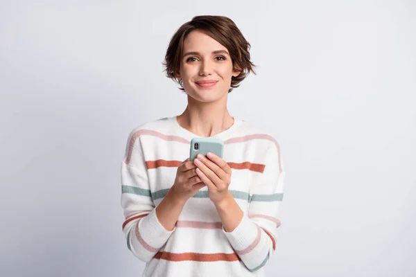 Foto de encantadora mujer joven dulce vestido a rayas suéter que sostiene el dispositivo moderno aislado fondo de color gris —  Fotos de Stock