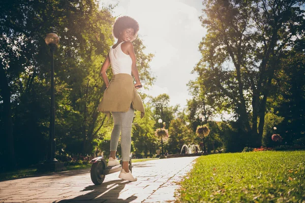 Foto retrato de chica brillante mirando por encima del hombro montar e-scooter en el sol en el parque —  Fotos de Stock