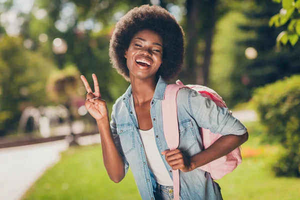 Zdjęcie portret czarnej oskórowanej dziewczyny uśmiechniętej pokazując znak V z dwoma palcami śmiejąc się nosząc dżinsową koszulę różowy luźny plecak — Zdjęcie stockowe