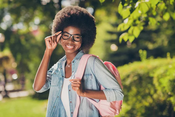 Zdjęcie portret dość czarny skóra kręcone dziewczyna uśmiechając szczęśliwie sobie dżinsy casual zamyka dotykając okularów utrzymanie różowy worek — Zdjęcie stockowe