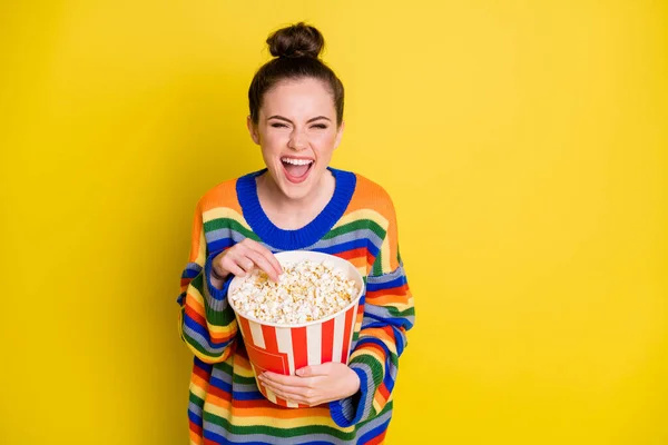 Porträt von ziemlich netten brünetten Mädchen essen Popcorn tragen Regenbogen-Pullover isoliert auf leuchtend gelbem Hintergrund — Stockfoto