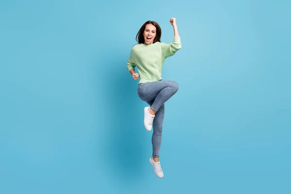Teljes testhossz fotó vidám jumping lány visel alkalmi ruhák kiabálva boldogan tartja fel a kezét, mint győztes elszigetelt élénk kék háttér — Stock Fotó