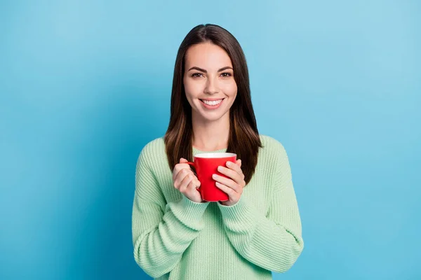 Foto retrato de menina morena mantendo quente xícara de chá sorrindo usando jumper verde isolado no fundo de cor azul vibrante — Fotografia de Stock