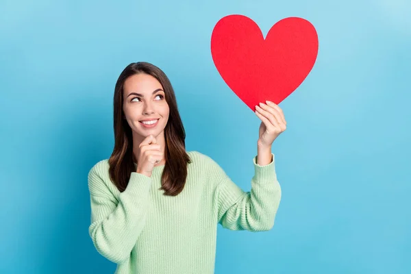 Retrato fotográfico de la astuta chica hermosa manteniendo el corazón rojo sobre la cabeza tocando la cara sonriendo mirando hacia arriba aislado sobre un vibrante fondo de color azul —  Fotos de Stock