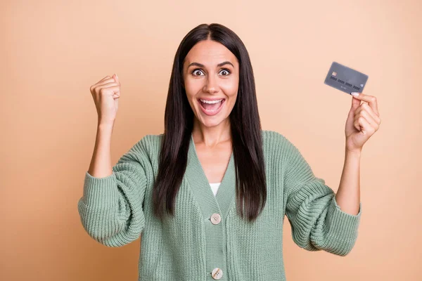 Φωτογραφία του κατάπληκτος ευτυχισμένη νεαρή γυναίκα κατέχουν πιστωτική κάρτα αυξήσει τις γροθιές κερδίσει χρήματα λαχείο απομονώνονται σε παστέλ μπεζ χρώμα φόντο — Φωτογραφία Αρχείου