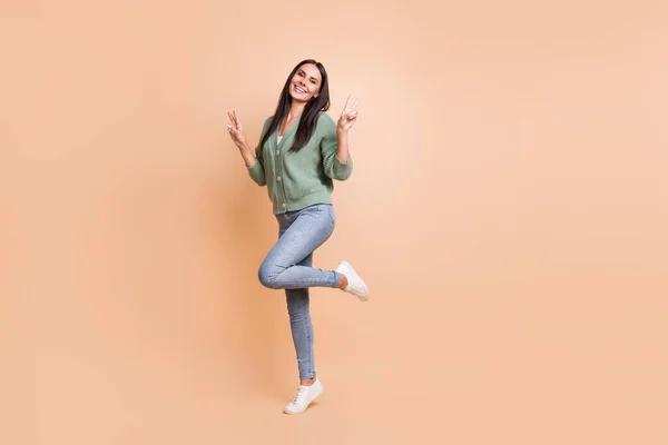 Volledige lengte foto van charmante vrolijke vrouw tonen twee v-tekens hallo staan een been geïsoleerd op beige kleur achtergrond — Stockfoto