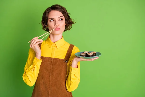 Foto de mente inteligente menina segurar pauzinhos prato sushi olhar espaço vazio desgaste camisa amarela geral isolado cor verde fundo — Fotografia de Stock