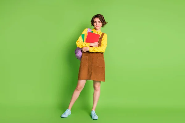 Full size photo of pretty cute brunette girl stand hold copybooks rucksack wear brown dress sneakers isolated on green background — Stock Photo, Image