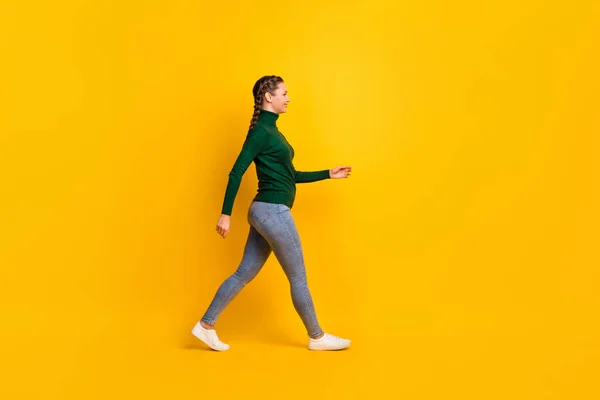 Foto de cuerpo entero del estudiante femenino con trenzas en jeans cuello alto caminando hacia adelante aislado sobre fondo de color amarillo vibrante —  Fotos de Stock