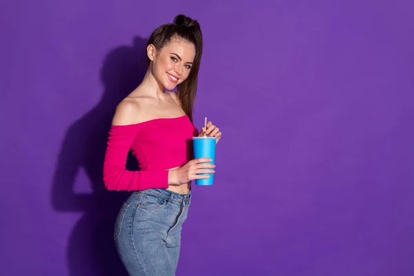 Profil fotografie okouzlující mladá dáma držet pohár sláma prázdný prostor oblečení džíny růžová odkrytá ramena vrchol izolované fialové barvy pozadí — Stock fotografie