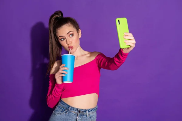 可爱女孩拿着杯子电话的照片让自己穿牛仔裤粉红肩膀顶部孤立的紫色背景 — 图库照片