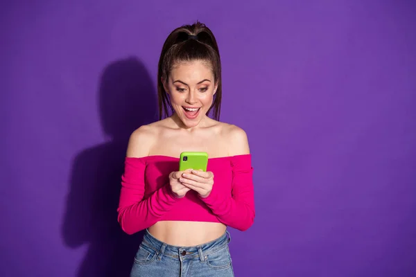 Photo of lovely girl trzymać telefon przeglądać internet zdumiony nosić dżinsy różowy odkryte ramiona top odizolowany fioletowy kolor tła — Zdjęcie stockowe