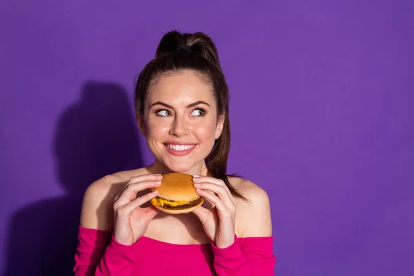 魅力的な空腹陽気な女の子食べるホットバーガー思考コピースペース隔離された明るい紫色の背景 — ストック写真