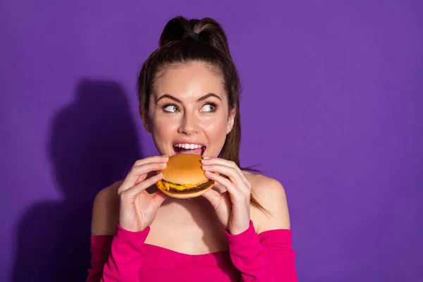 Közelkép portré vonzó vidám lány eszik friss forró burger gondolkodás másolás tér elszigetelt fényes lila színű háttér — Stock Fotó