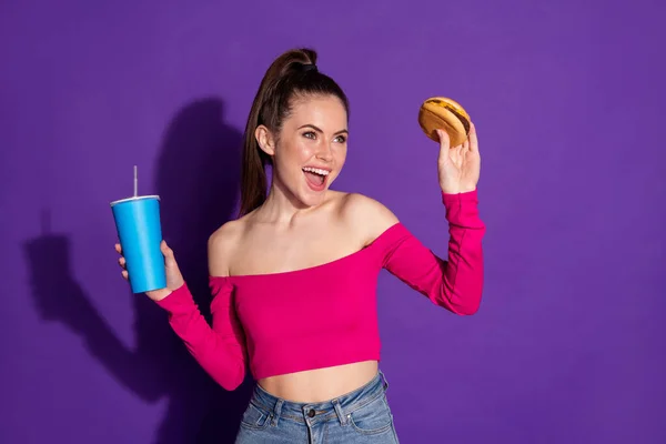 Portré vonzó vidám barna hajú lány eszik burger ivókóla élvezi elszigetelt fényes lila színű háttér — Stock Fotó
