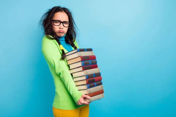 Foto de morena tranças cabelo jovem segurar livros pesados usar camisa verde calças amarelas isoladas no fundo de cor azul vívido — Fotografia de Stock