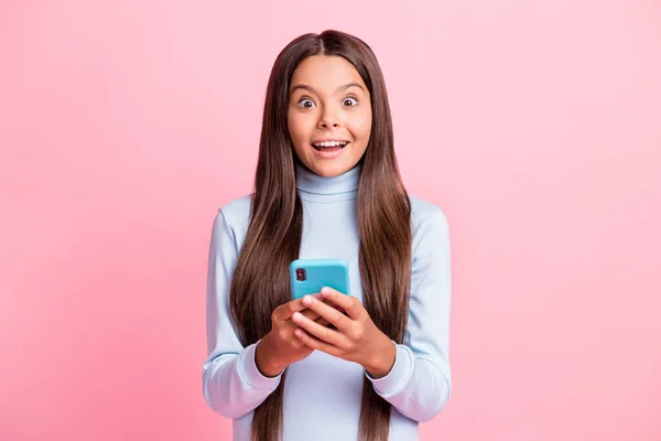 Portret van vrij verbaasd vrolijke bruin-harige meisje met behulp van apparaat met plezier geïsoleerd over roze pastel kleur achtergrond — Stockfoto