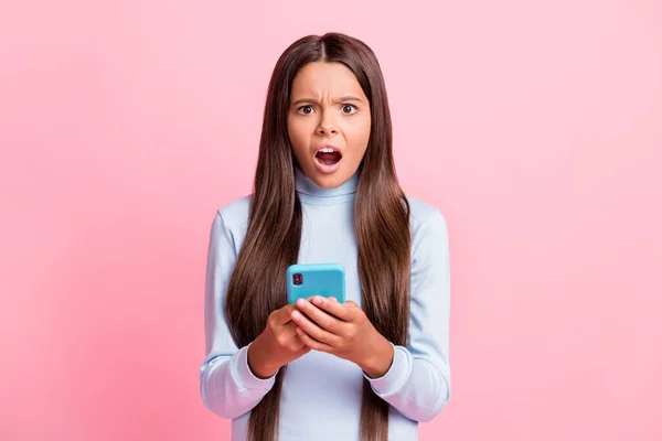 Retrato de muito indignado menina de cabelos castanhos com raiva usando gadget navegando notícias falsas isoladas sobre fundo cor pastel rosa — Fotografia de Stock