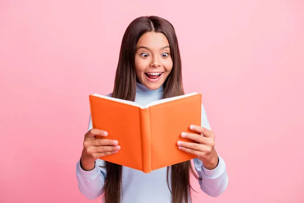 Retrato de encantador surpreendido alegre menina de cabelos castanhos lendo livro interessante isolado sobre cor pastel rosa fundo — Fotografia de Stock