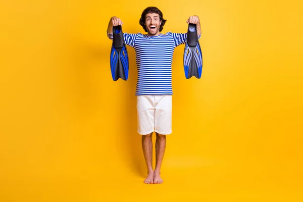 Foto de comprimento total de cara louco segurar barbatanas mergulho desgaste azul branco camisa shorts descalço isolado no fundo de cor amarela — Fotografia de Stock