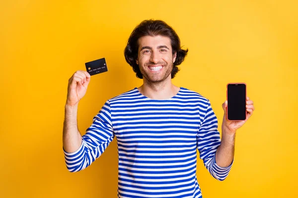 Portret van positieve man hold smartphone toon credit card slijtage nautische witte vest geïsoleerd op glans gele kleur achtergrond — Stockfoto