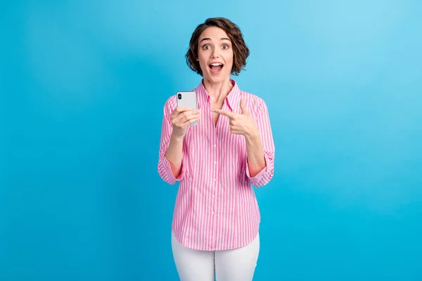 Foto de sorprendida chica dedo dedo dedo teléfono inteligente usar pantalones blancos rosados aislados en fondo de color azul — Foto de Stock