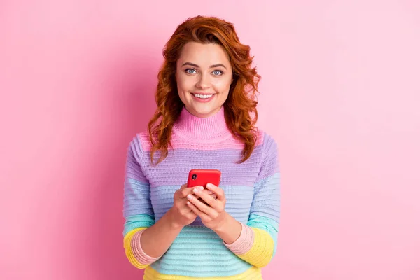 Foto retrato de una mujer sonriente sosteniendo el teléfono en dos manos aisladas sobre fondo de color rosa pastel — Foto de Stock