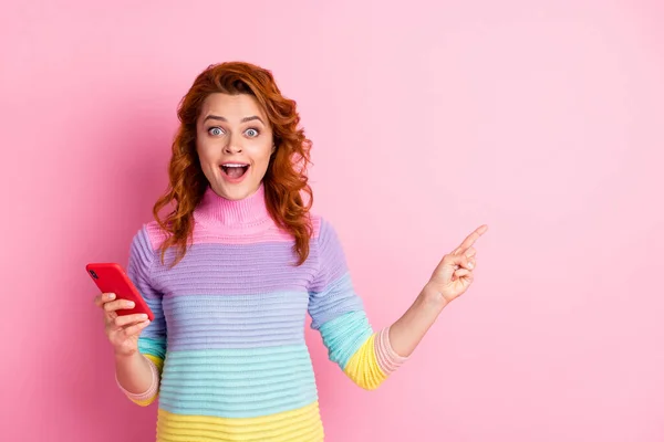 Foto ritratto di donna eccitata che tiene il telefono in una mano che punta il dito verso lo spazio vuoto isolato su sfondo rosa pastello — Foto Stock